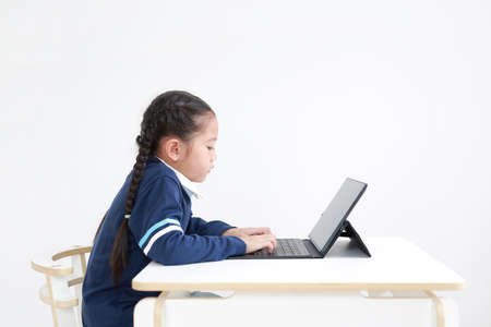 Asian little kid girl in school uniform using laptop on table isolated on white background, Studio...