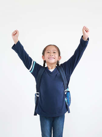 Happy asian little child girl in school uniform with backpack raise hands up isolated on white background. Studio shot.の写真素材