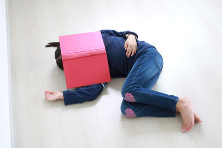 Portrait asian little kid girl with book cover his face and sleeping on wood laminate flooring. Education conceptの写真素材