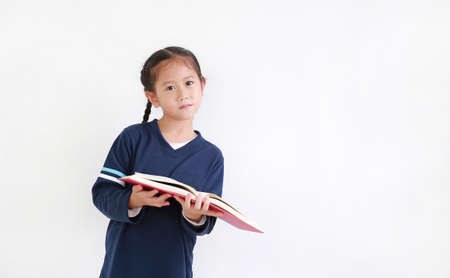 Portrait asian little girl in casual school uniform holding open book with looking camera isolated...