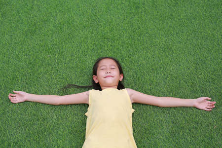 Close eyes little Asian child girl with two ponytail hair lying on green grass in the garden.の写真素材