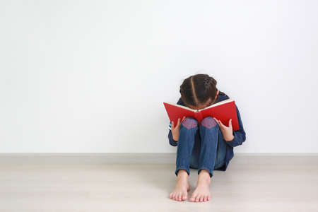 Asian little child girl tired after read a book while placed book cover his face sitting on wooden...