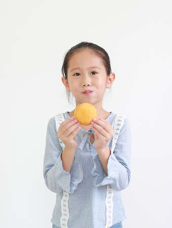 Portrait of happy asian little child girl hold and eating Custard Cake isolated on white background.の写真素材