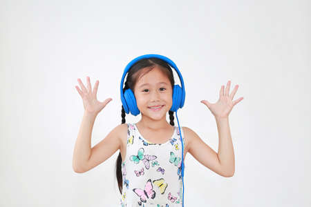 Happy asian little child girl listening music by blue headphones and looking at camera on white backgroundの写真素材