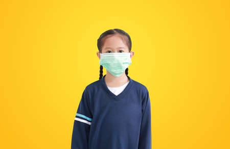 Portrait asian little child girl with wearing medical mask isolated on yellow backgroundの写真素材