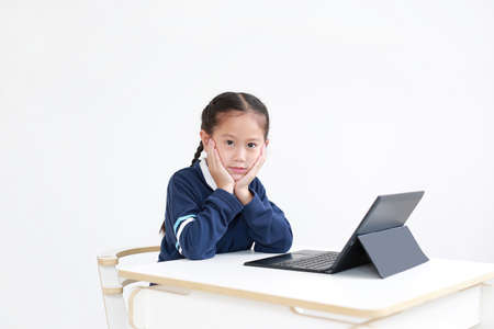 Portrait asian little child girl in school uniform using laptop on table isolated on white...