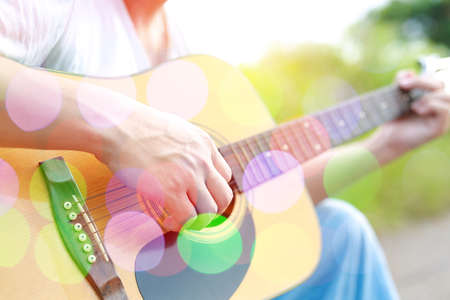 Colored bokeh image of male hand playing on acoustic guitar.