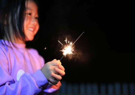 Little Asian child girl enjoy playing firecrackers. Focus at fire sparklers.