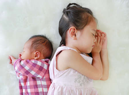 Asian older sister and newborn baby boy sleeping together on white fur background.の写真素材