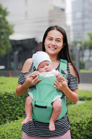 Asian mother carrying her infant baby by hipseat outdoor.