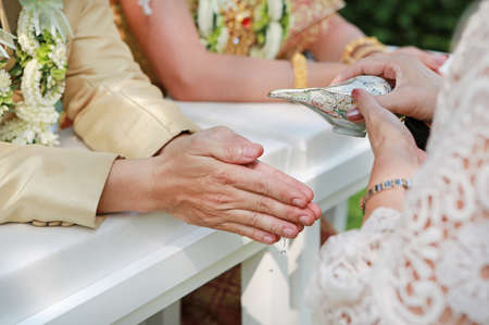 Hands pouring blessing water into groom's hands, Thai wedding.の写真素材
