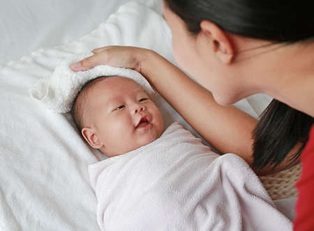 Mother rub the body dry for smiling little baby boy in towel lying on bed after bath.