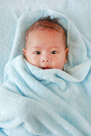 Portrait of Infant baby boy in towel roll looking at camera lying on bed after bath. Above view.の写真素材