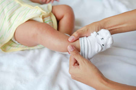 Close-up mother hands trying to put a socks for her infant baby on the bed.