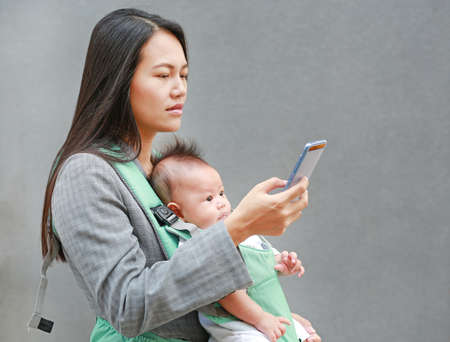 Portrait of business woman working by smartphone with carrying her infant.