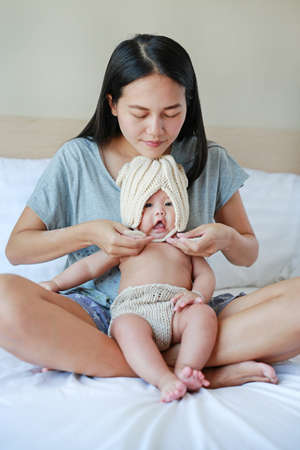 Mother put on some knit clothes to her baby on the bed.