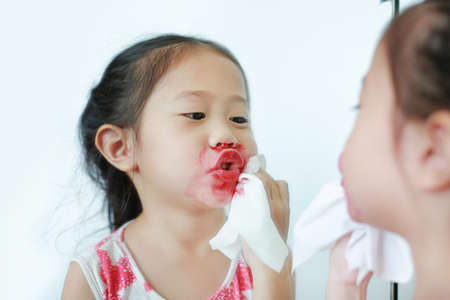 Adorable little Asian child girl trying mother's lipstick near a mirror.の写真素材