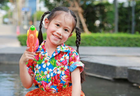 Cheerful kid girl playing water gun at Songkran festival on summer season in thailand (Thai new year - water festival).の写真素材