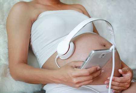 Hands of pregnant woman holding headset putting headphones to belly, motherhood concept.の写真素材