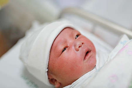 Open eyes newborn infant in the blanket at delivery room.の写真素材