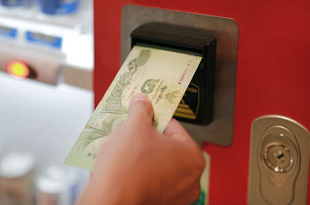 Close up hand inserting banknote into the machine for buying food or drink.