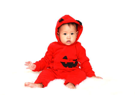 Adorable little baby boy in red halloween costume sitting on fur over white background.