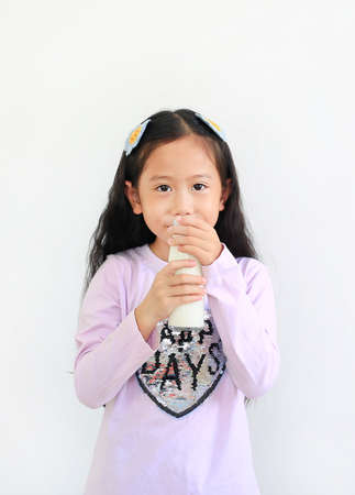 Cheerful asian little child girl drinking milk from glass bottle isolated on white background.の写真素材