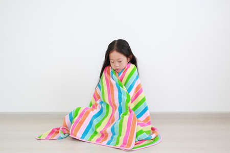 Asian little kid girl sitting wrapped covered in soft multicolor blanket in the roomの写真素材