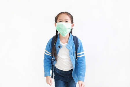 Portrait asian little kid girl in casual school uniform wearing medical mask with backpack isolated on white background. Studio shotの写真素材