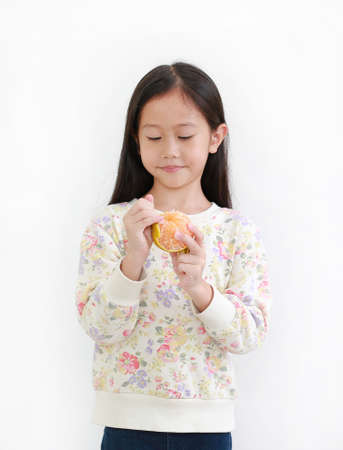 Portrait of little asian girl peeling orange on white background