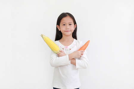 Little asian girl holding carrot and sweet corn gesture cross one arm standing isolated on white background. Kid and vegetable conceptの写真素材