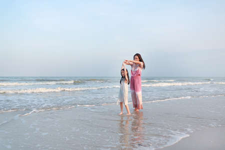 Asian mom and daughter relax and dancing together on sea beach on vacation time.の写真素材