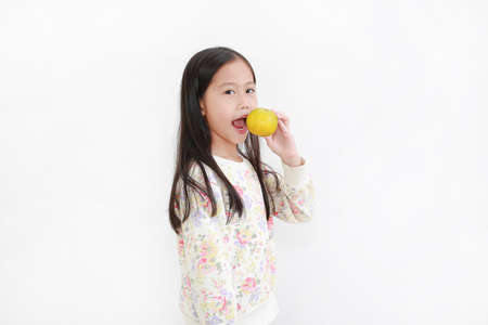 Portrait little asian kid girl holding not peeled orange fruit and gesture eating over white...