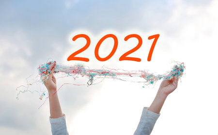 Hands lift up a multi color paper spray over sky background with text 2021. Decoration for new year...