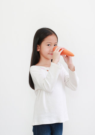 Portrait of asian little kid girl making long nose with carrot isolated on white backgroundの写真素材