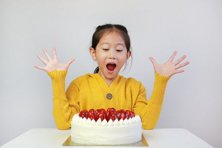 Excited asian little girl with strawberry cake. Kid with happy birthday cake on the table