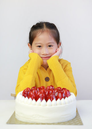 Cute young asian little girl with strawberry cake. Kid with happy birthday cake on the tableの写真素材