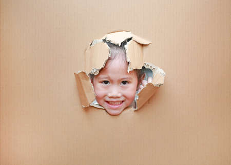 Happy Asian kid girl looking through hole on cardboard with copy space.の写真素材