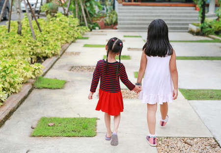 Rear view of Sister hold hands with small children walking on the road garden.の写真素材