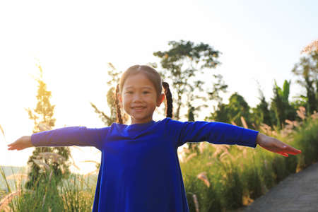 Portrait of smiling little Asian child girl opened her arms in field at sunset.の写真素材