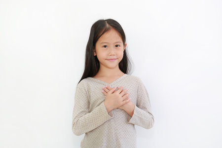 Portrait of Asian little girl holding hands on heart gesture of love. Kid place arms on chest...