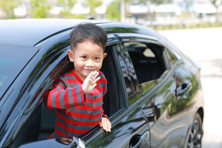 Asian little boy in car smiling and looking camera sitting on a seat of car waving goodbye.の写真素材
