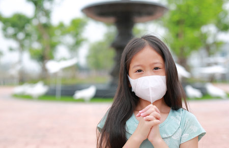 Asian little girl child wearing face mask and pray gesture for stop covid-19 during coronavirus outbreakの写真素材