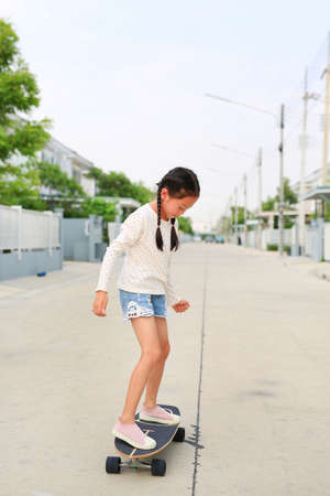 Asian little girl child skating on a skateboard. Kid riding on skateboard outdoors at the street....