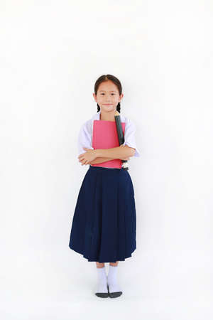 Asian little young girl child in Thai school uniform standing with hugging a book and big pencil...