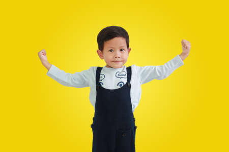 Asian little boy raising hands up for strong gesture isolated on yellow background.の写真素材