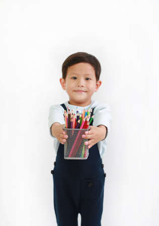 Asian little boy giving a basket of colored pencils for you against white background. Focus  at color pencil in his handsの写真素材
