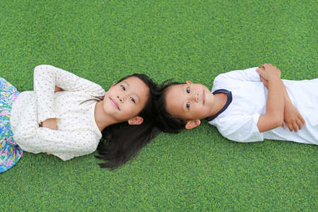Asian little boy and girl child lying on green grass background together with looking camera.の写真素材