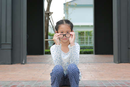 Asian girl child sitting in the garden while take off glasses and looking at camera.の写真素材