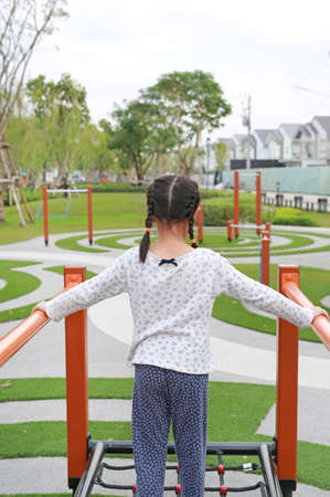 Asian young girl playing on equipment at a playground. Rear view.